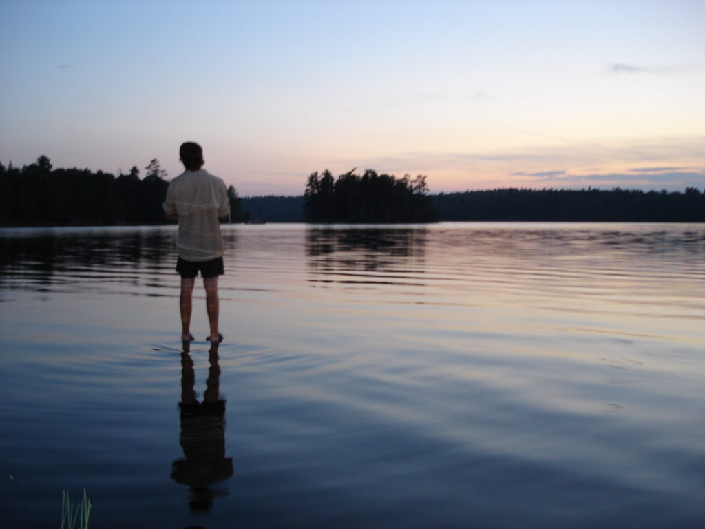 Young man staring out across a still lake.